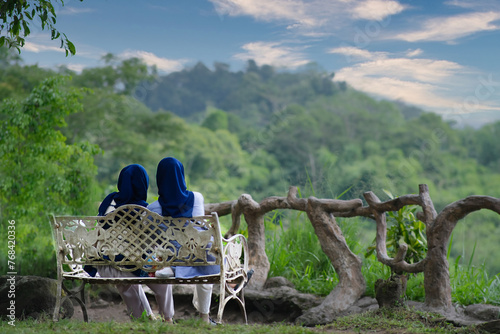 Two moslem sisters sitting side by side in a wrought iron bench enjoying the view photo