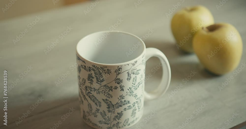 Close Up Shot Of Water Pouring Into Cup. Yellow Apples In The Background Close Up Shot Of Water Pouring Into Cup. Yellow Apples In The Background