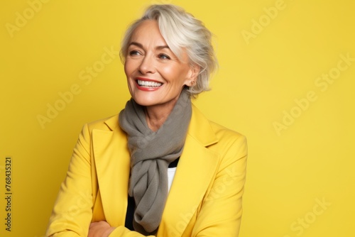 Portrait of smiling senior woman in yellow coat and scarf on yellow background