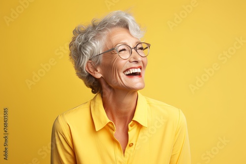 Portrait of a happy senior woman in glasses on a yellow background