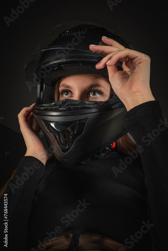 Beautiful young girl a motorbiker in black safe motorbike helmet posing on gray background.