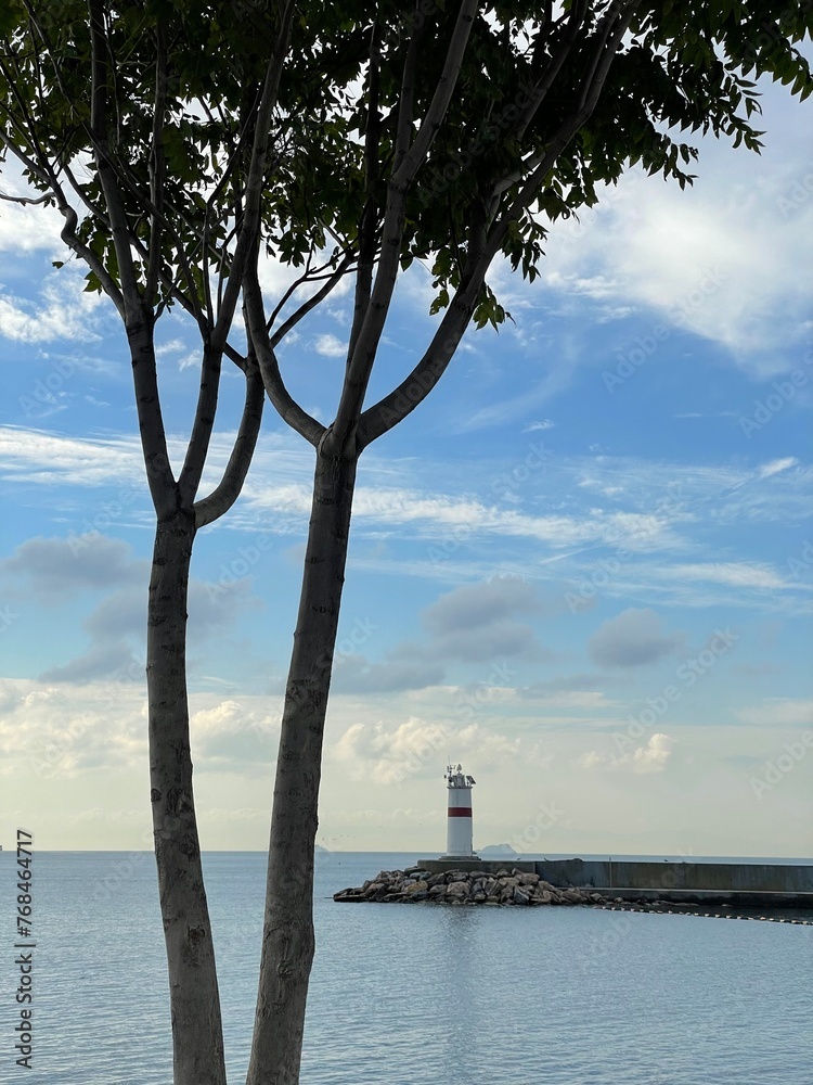 Fototapeta premium Lighthouse in the middle of the sea with trees and blue sky