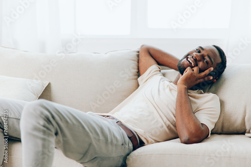 Happy African American man sitting on a black sofa, holding a mobile phone and using wireless technology for a video call He is relaxed and confident, enjoying his leisure time at home The modern