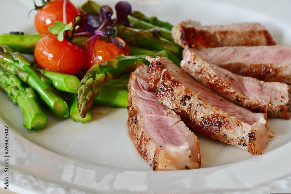 Grilled duck breast with asparagus and cherry tomatoes on white plate
