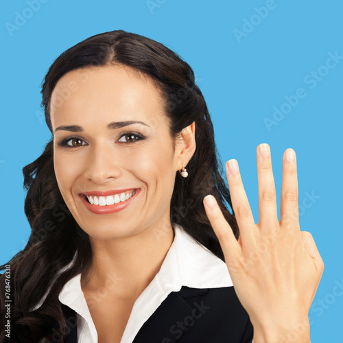Businesswoman wear black confident suit showing four fingers, isolated against blue background. Happy smiling gesturing brunette woman at studio. Business success ad concept. Square composition image.