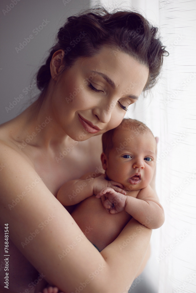 beautiful family portrait mum cuddles her newborn daughter standing by the window in the room in the afternoon. beautiful family portrait mum cuddles her newborn daughter standing by the window in the room in the afternoon.