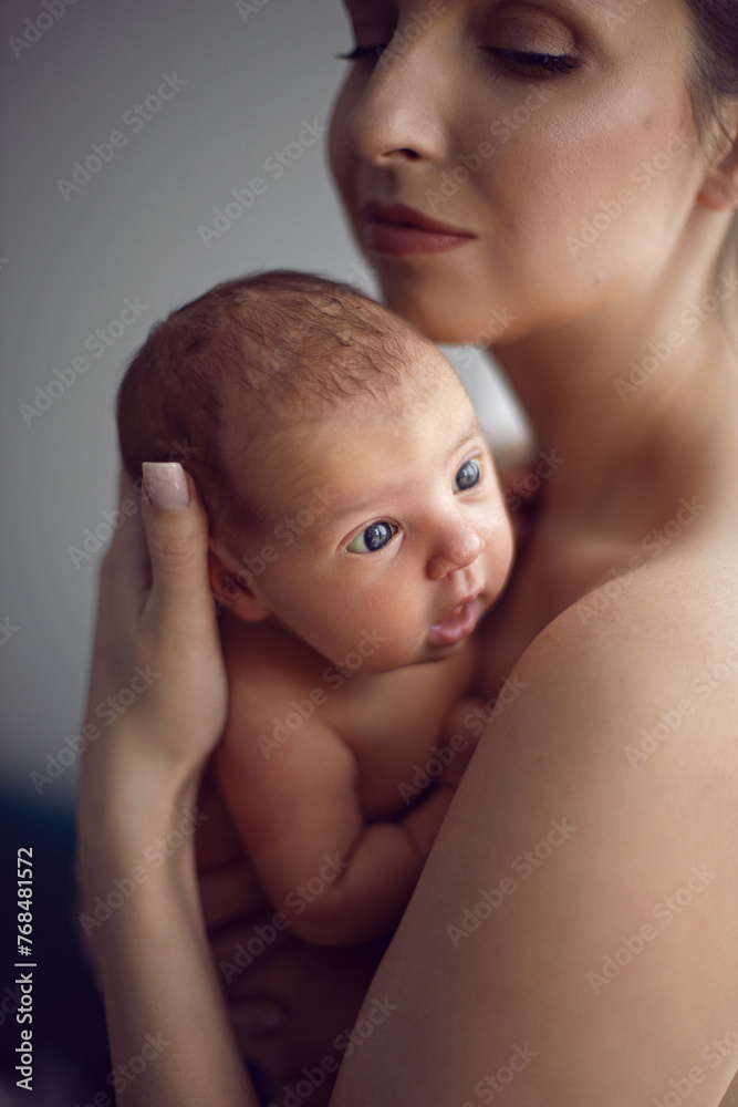 beautiful family portrait mum cuddles her newborn daughter standing by the window in the room in the afternoon. beautiful family portrait mum cuddles her newborn daughter standing by the window in the room in the afternoon.