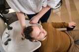 Barber shampooing washing a male clients head in the sink.