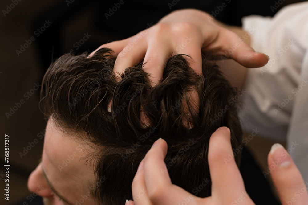 Naklejka premium Haircut of a visitor in a barbershop. Hair styling with a hand, combing the client's hair by a stylist.