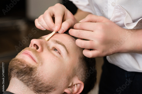 Hair removal procedure in a barbershop. Eyebrows hair wax removal.