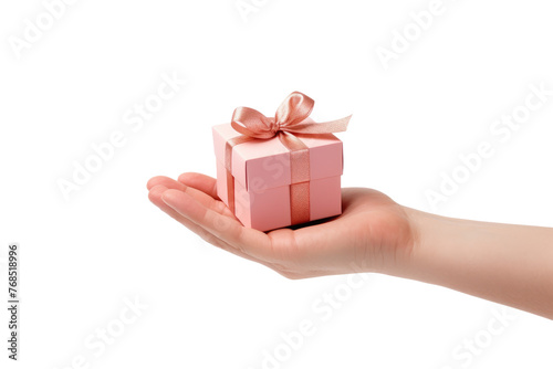 A hand is shown holding a pink gift box with a decorative bow on top. The box appears to be small in size, and the hand is delicately gripping it. Isolated on a Transparent Background PNG. © Haider