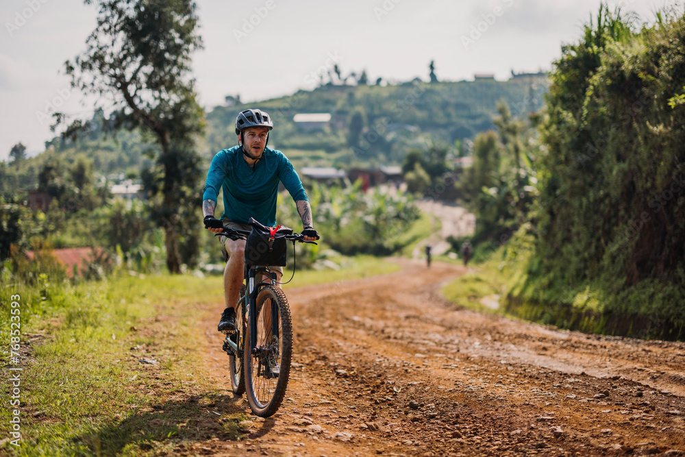 male cyclist bikes up dirt road on Congo Nile Trail in Rwanda male cyclist bikes up dirt road on Congo Nile Trail in Rwanda