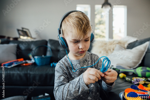 Close up of small boy wearing headphones in front of messy couch photo