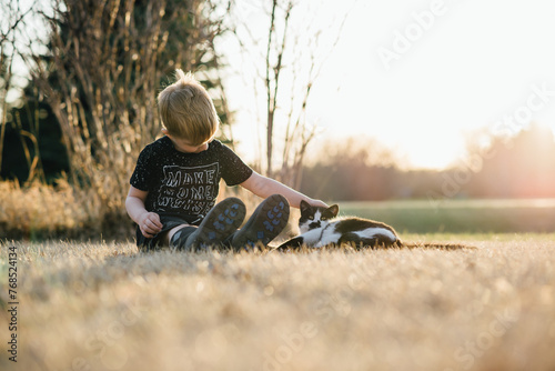 Low front view of young boy sitting on ground next to happy cat