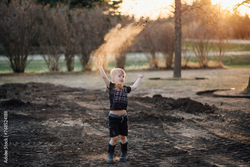 Wide front view of young boy playing outside and throwing dirt in yard photo