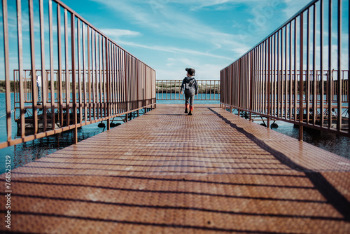 Toddler boy walking down a dock at a lake in summer photo