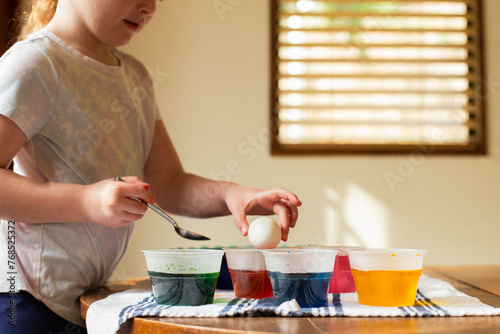 Little girl dyeing Easter eggs at kitchen table photo