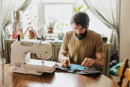 Man sits at kitchen table with sewing machine patching work pants photo