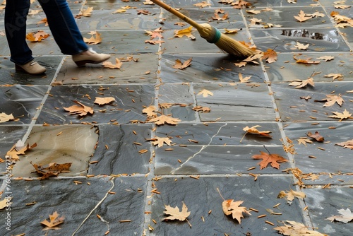 woman sweeping fallen leaves off a stone tiled patio © altitudevisual