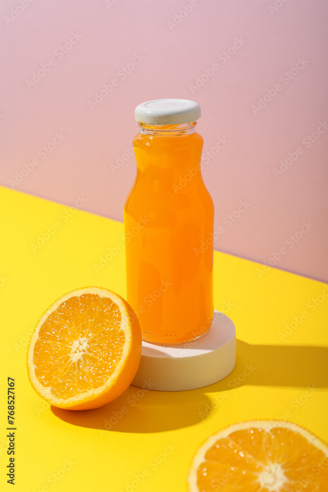 Glass bottle with juice and oranges on pink background Glass bottle with juice and oranges on pink background