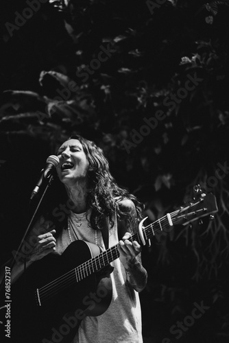 Young woman singer, sings into a microphone and plays the guitar.
