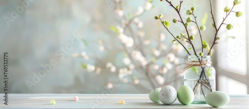A clear glass vase filled with colorful Easter eggs is placed on top of a wooden table. In the background, green buds on branches add to the festive decor.