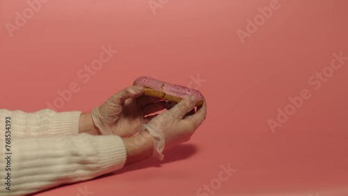 Hands braking berry eclair in two pieces. Pink background. China. 