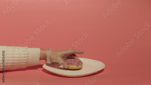 Close up of a hand putting pink donut on the white plate over the pink background. Cooking. Desert. Servicing. 
