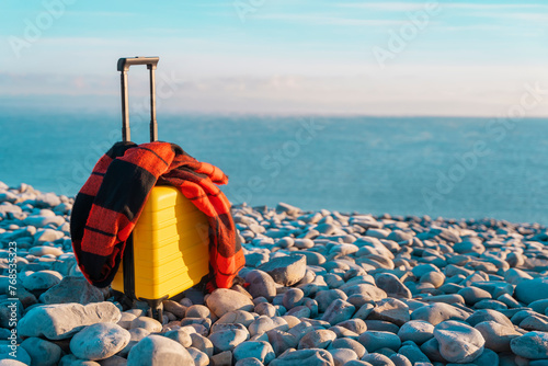 Yellow Suitcase with an orange scarf on the seaside against the sea. Travel concept. © Iryna