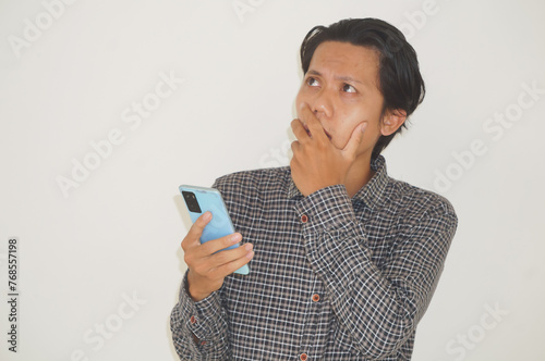 Young Asian man thinking about something while holding mobile phone. isolated white background photo