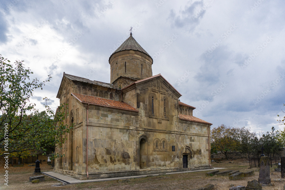 Autumn view of courtyard and Ertatsminda church. Colorful trees, leaves and grass. Beautiful bas-reliefs on the walls of the church. Cross on the top. Georgia Autumn view of courtyard and Ertatsminda church. Colorful trees, leaves and grass. Beautiful bas-reliefs on the walls of the church. Cross on the top. Georgia
