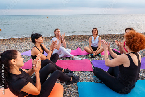 Top view of group of young-adult multi-racial women are sitting on sports mats and talking and applaud each other. Concept of female circle of communication and outdoor yoga class