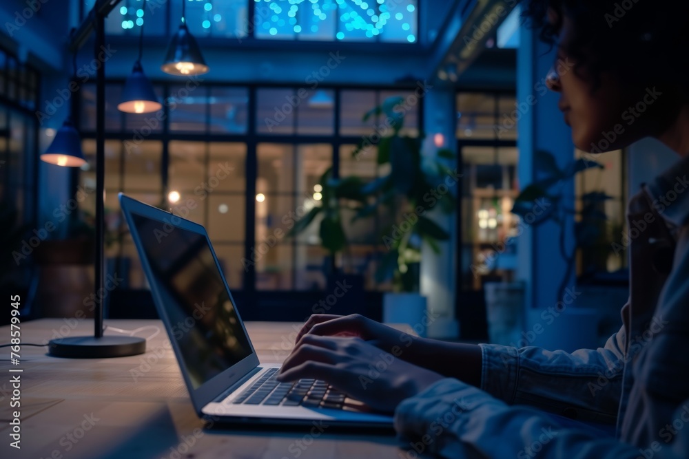 person using laptop in dimly lit openplan office area person using laptop in dimly lit openplan office area
