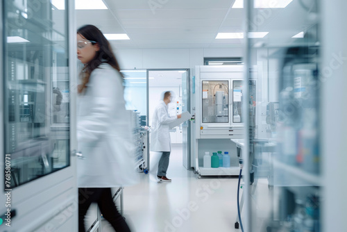 a modern electrochemistry lab  scientists wearing white lab coats are seen at work. A female scientist is busy working a male scientist is walking a with documents.