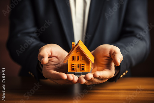 A businessman in a suit holds a model of a house on his palms. Male hands holding house model .