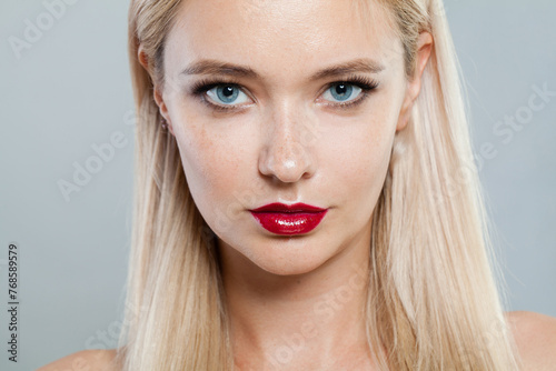 Close-up photo of young woman with make-up and long blonde hair against white studio wall background