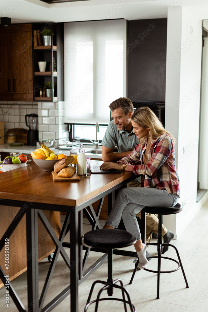 Cheerful couple enjoys a light-hearted moment in their sunny kitchen, working on laptop surrounded by a healthy breakfast Cheerful couple enjoys a light-hearted moment in their sunny kitchen, working on laptop surrounded by a healthy breakfast