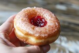 hand holding halfeaten jelly donut, red filling visible