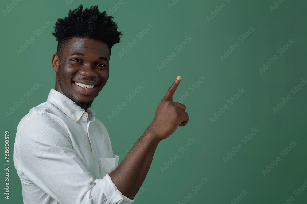 African american male person with toothy smile on face pointing with index finger on empty space over green background. Handsome young guy indicating place for advertising text in studio African american male person with toothy smile on face pointing with index finger on empty space over green background. Handsome young guy indicating place for advertising text in studio
