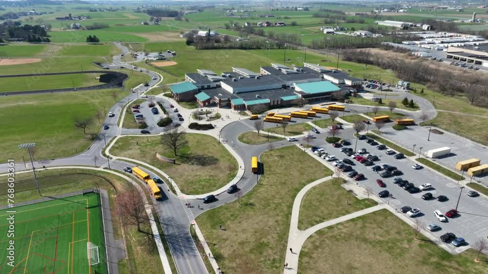Yellow School bus and Cars picking up students of High School in American Suburb. Green countryside fields in USA. Aerial top down orbit. Yellow School bus and Cars picking up students of High School in American Suburb. Green countryside fields in USA. Aerial top down orbit.