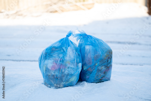 Two full blue plastic garbage bags placed on snow the roadside. Concept of recycling, public utilities, taking out a rubbish