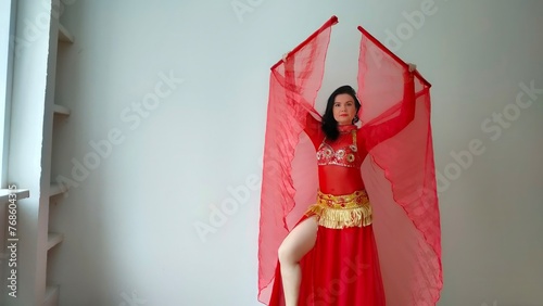 A dancer in a red suit is dancing with a red wings an oriental dance on a white background. Free space for text. Banner. A professional dancer dances oriental belly dance. Sexy woman in red dress