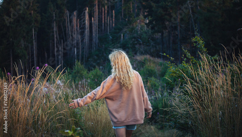Young Blonde Girl with Hoodie Walking in Dark Forest