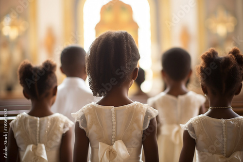 Gathering of black girls in formal attire standing around the church altar with candles and a crucifix. Back shot attending a religious service or ceremony. First communion concept.