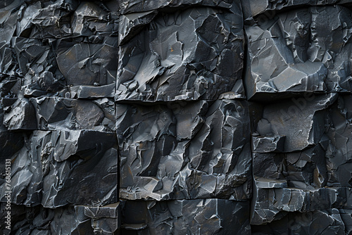 a close-up of a black stone wall made up of blocks of different sizes and shapes. The blocks are arranged in a grid pattern with some variation. 