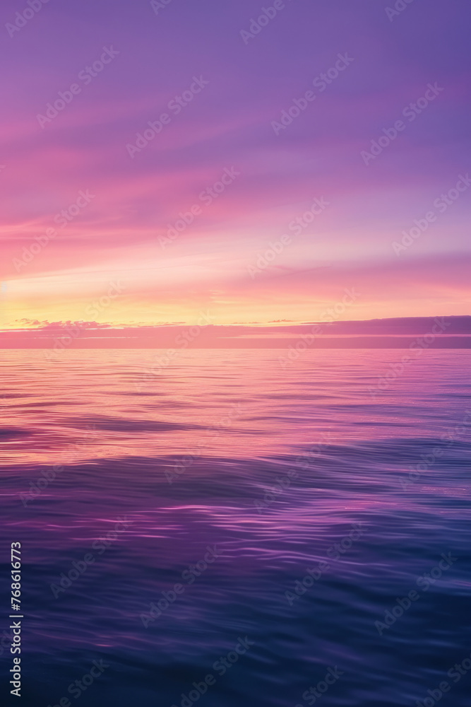 Tranquil seascape with smooth water surface and a vibrant sunset sky transitioning from pink to purple hues, reflecting on the calm ocean.