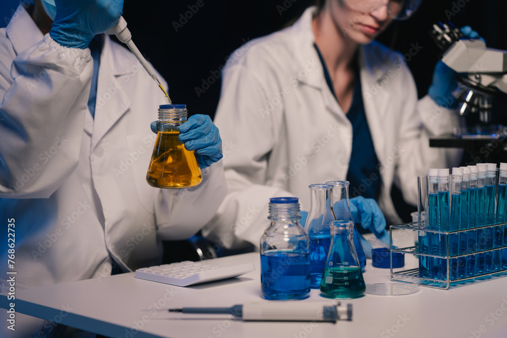 Fototapeta premium Life scientists researching in laboratory. Focused female life science professional pipetting solution into the glass cuvette. Healthcare and biotechnology concept.