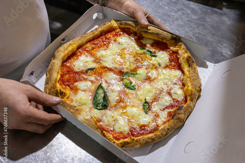 Pizza Margherita tradizionale napoletana con pomodoro, mozzarella e basilico mentre viene sistemata in un cartone da asporto di una pizzeria © Vincenzo VAD