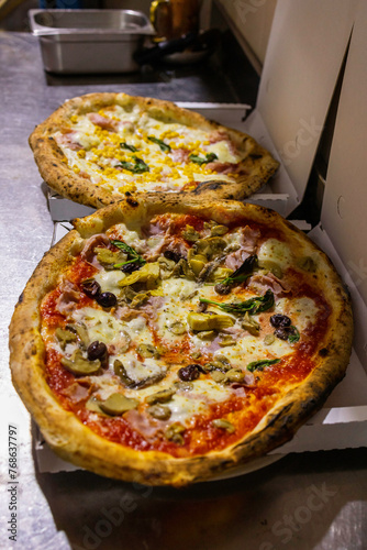 Pizze tradizionali napoletane con pomodoro, funghi, olive, prosciutto e mozzarella e con panna, prosciutto e mais pronte per essere chiude nei cartoni per l'asporto di una pizzeria