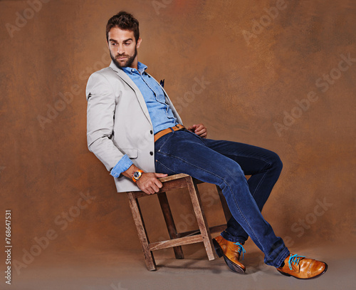Foto Fashion, serious and man in studio with trendy, stylish and classy suit on chair with confidence